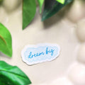 Sticker with 'dream big' text on a light background with green leaves