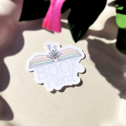 Sticker with a rainbow design and text which says "book nerd" on a light surface.