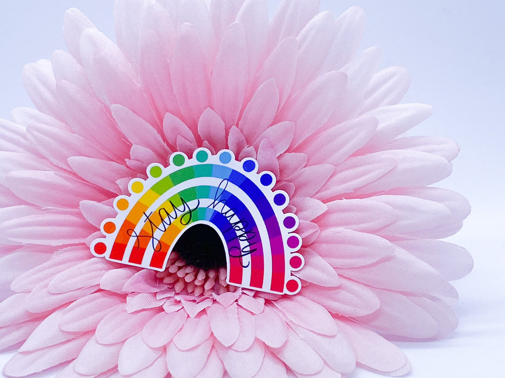 Rainbow "stay happy" sticker with a heart on a light pink flower