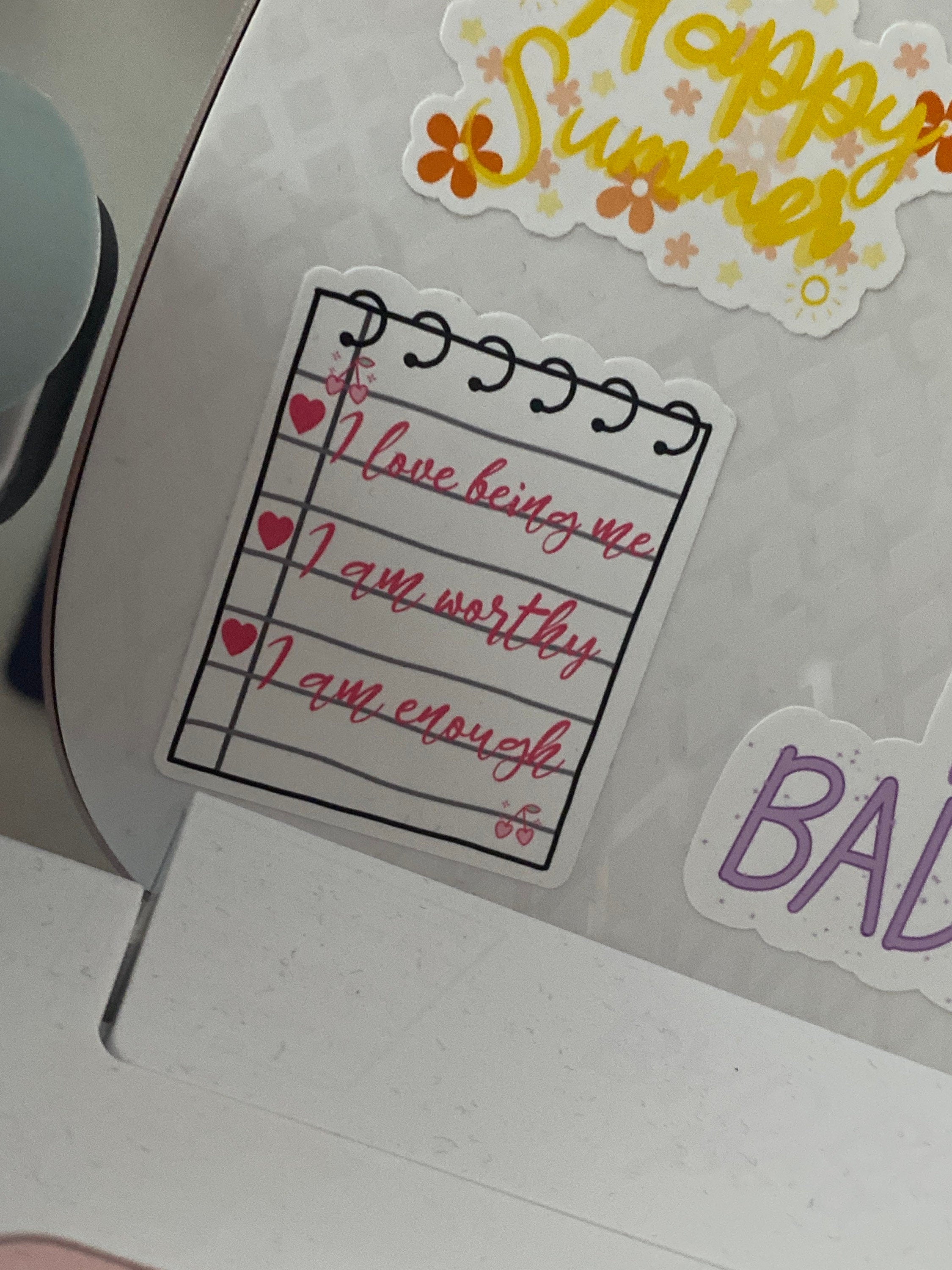 Motivational sticker with affirmations on a surface with other stickers.