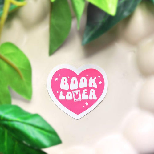 Heart-shaped 'Book Lover' sticker on a surface with green leaves in the background