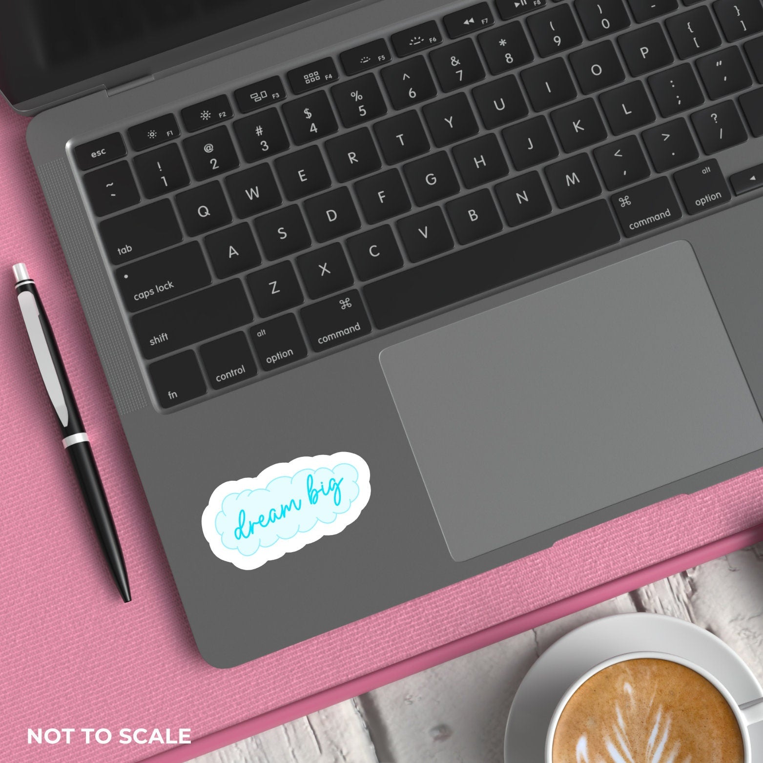 Laptop with 'dream big' sticker on pink surface with pen and coffee.